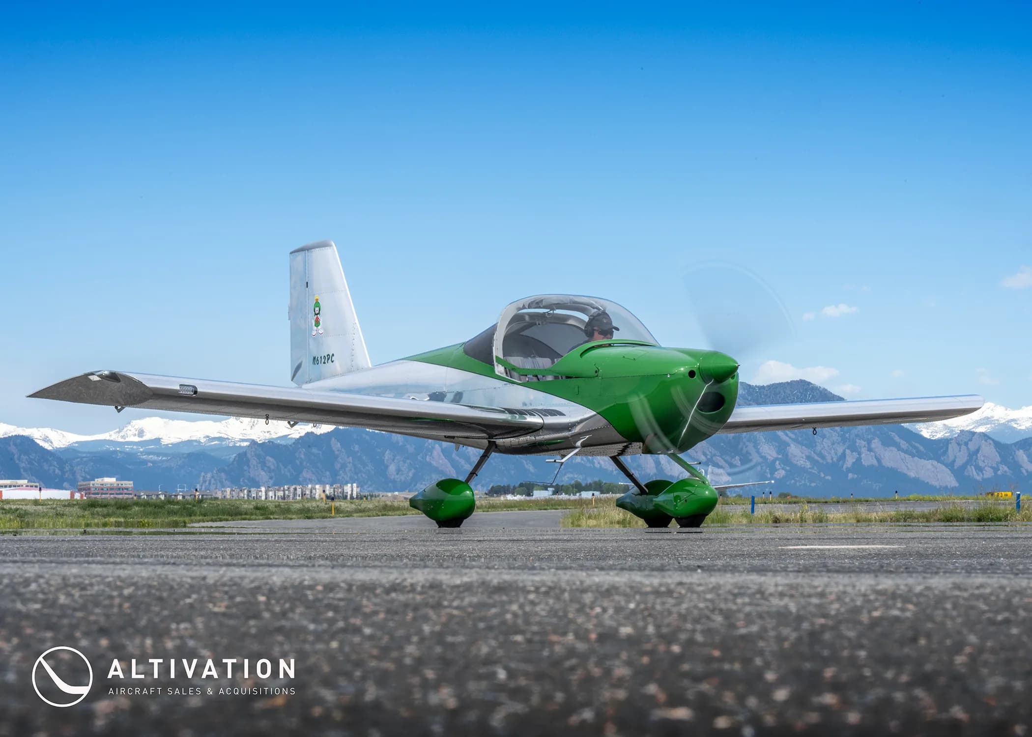A green and polished aluminum Vans RV-12 aircraft with registration N612PC on a runway with mountains in the background.