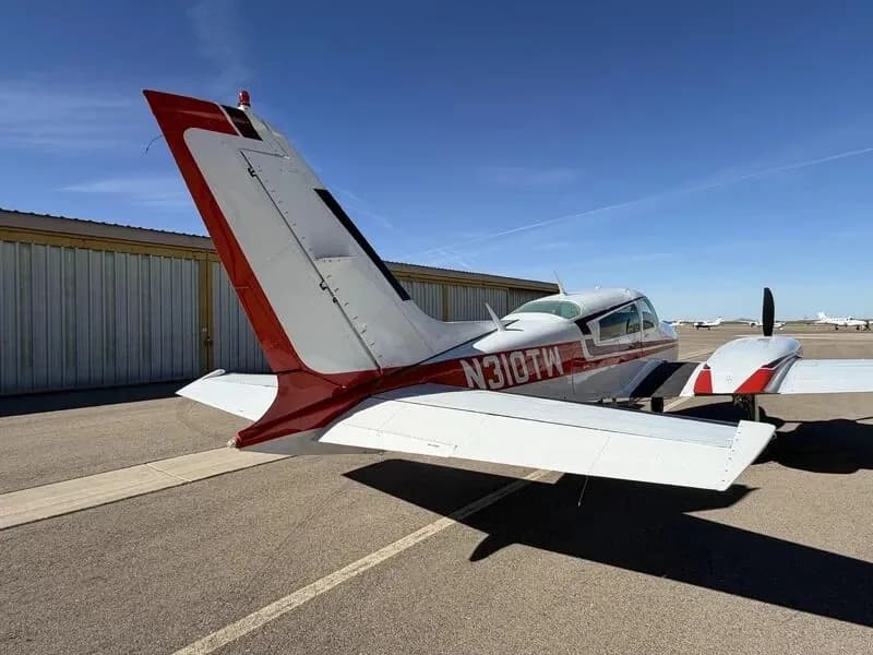 Rear view of a white and red Cessna 310 twin-engine aircraft showing the tail and right wing on an airfield.