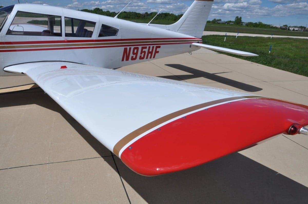 A close-up view of the right wing and tail section of a white aircraft with red and gold stripes.