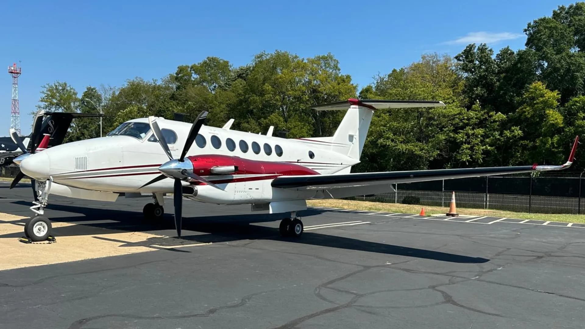 A white and red Beechcraft King Air N888FM parked on an asphalt tarmac with trees in the background.