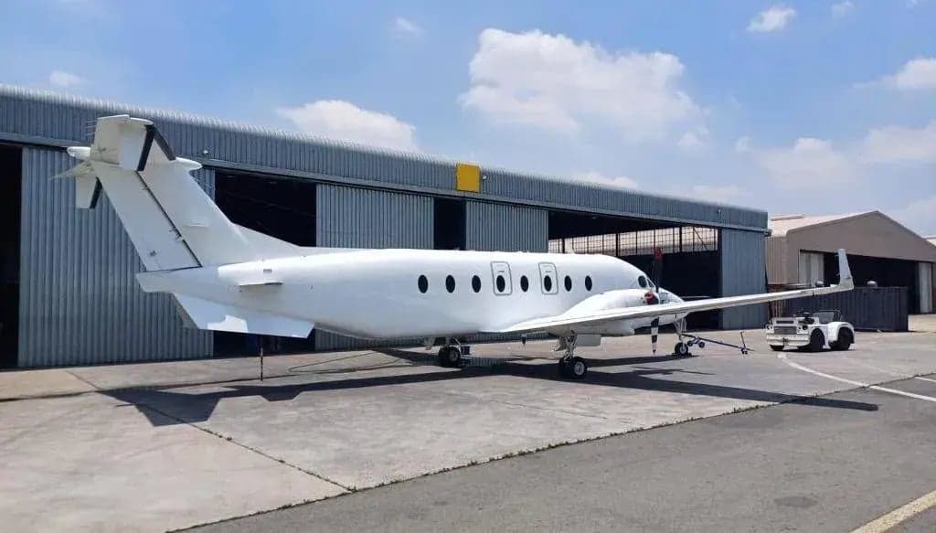 A side view of a white King Air aircraft parked in front of a hangar.