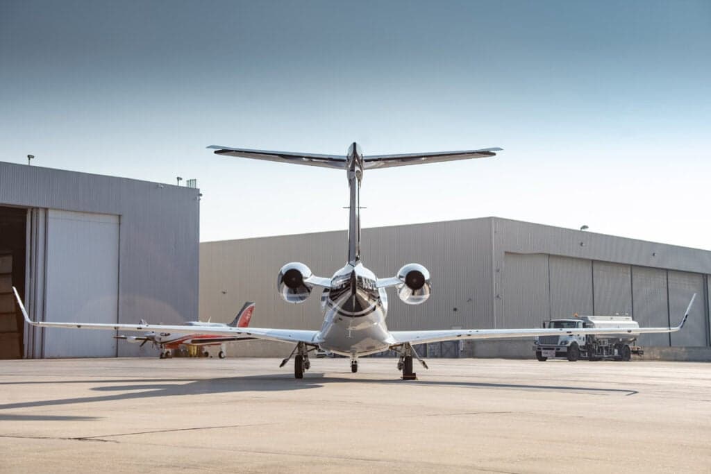 Rear view of a Phenom 300 aircraft parked on the tarmac in front of a hangar.