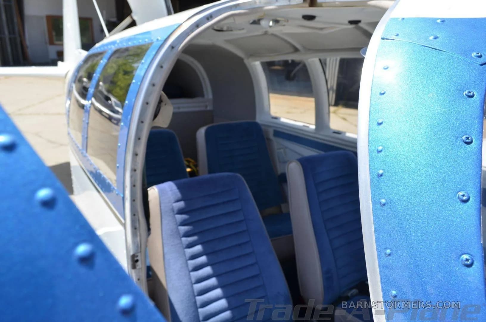 The open door of a small aircraft reveals its blue fabric interior seats and cabin space.