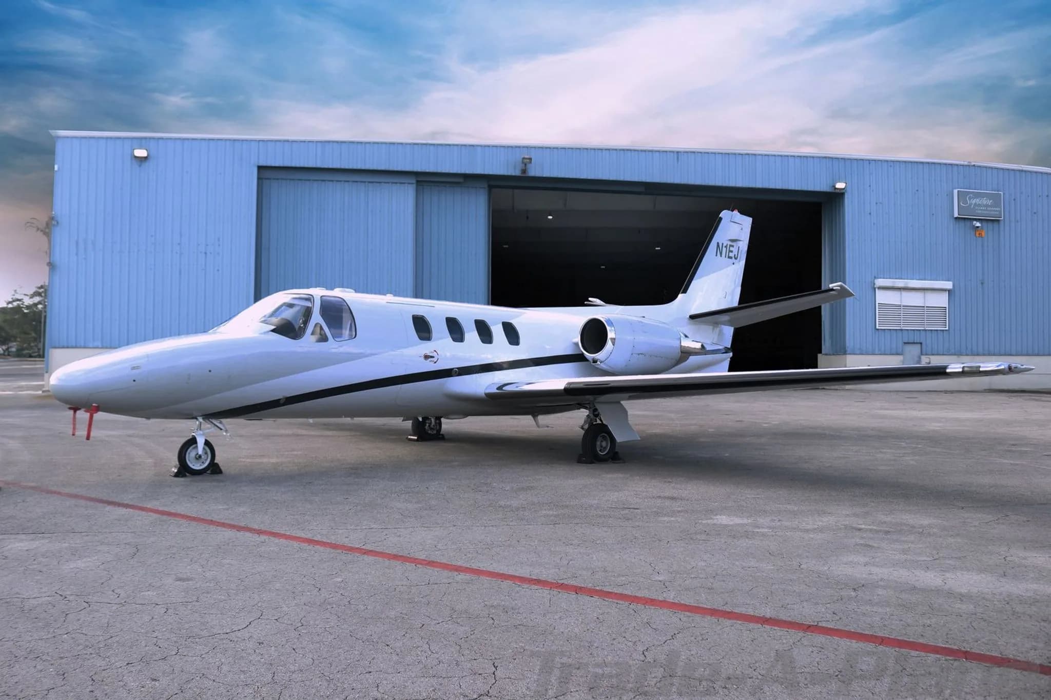 A white Cessna CitationJet N1EJ parked on an tarmac in front of a blue hangar.
