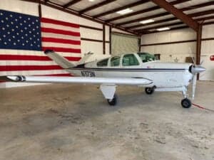 A Beechcraft Bonanza aircraft parked in a hangar with an American flag in the background.