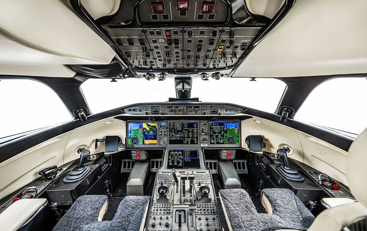 The modern cockpit of a business jet features multiple large display screens and a central control panel.