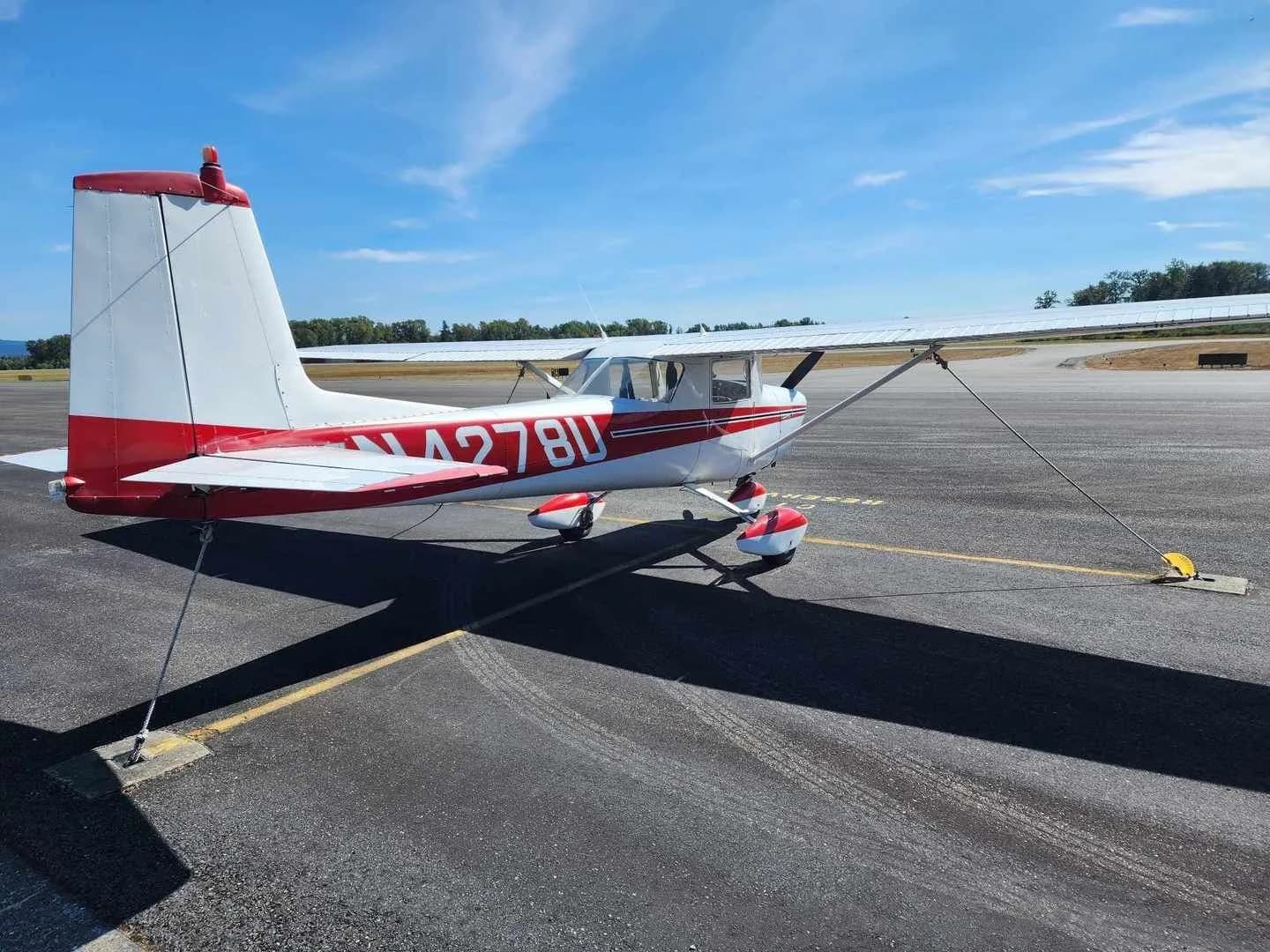 A white and red Cessna 150 aircraft with registration N4278U parked on an asphalt ramp under a clear blue sky, viewed from the rear-left.