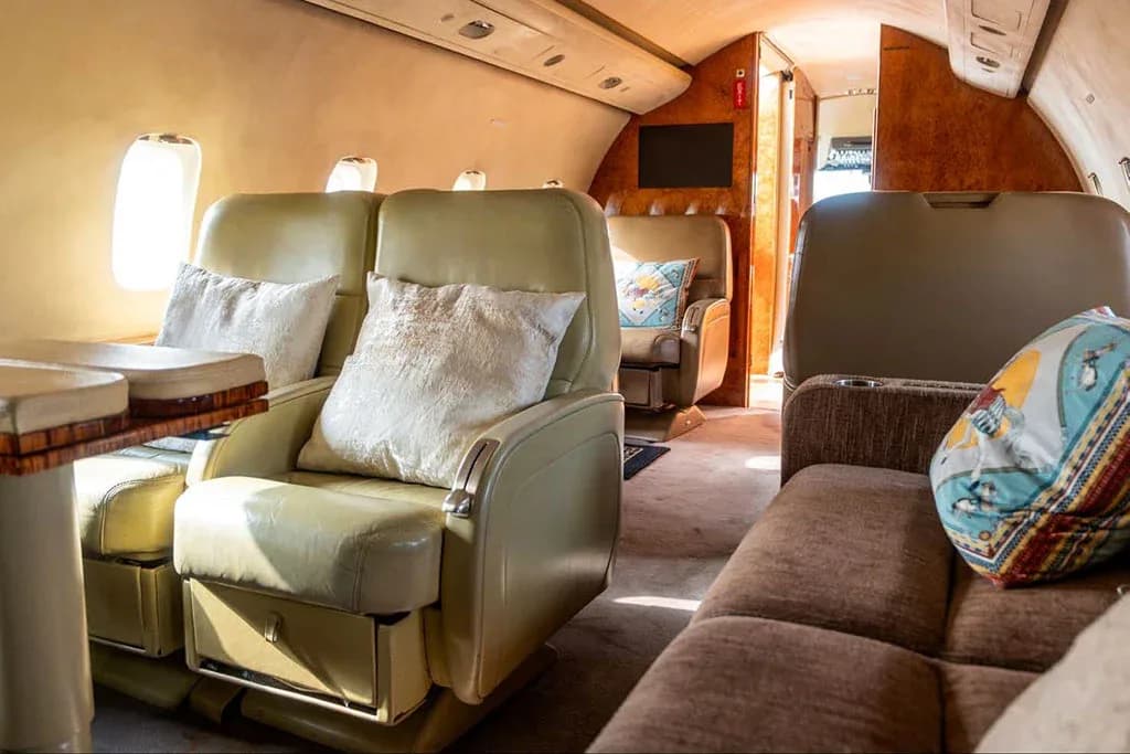 A private jet cabin interior featuring light green leather seats, a table, and a brown sofa.