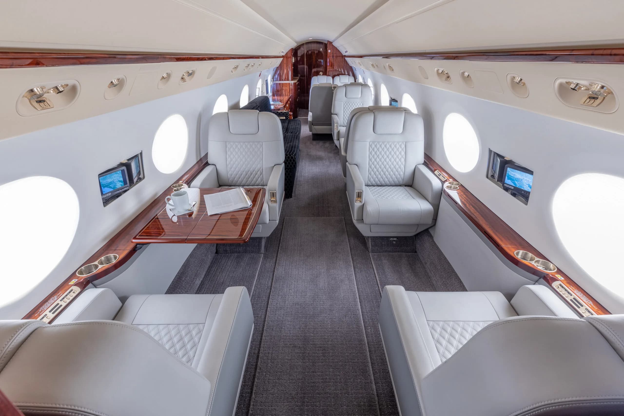 View of the aircraft interior with white leather seats and wood trim.