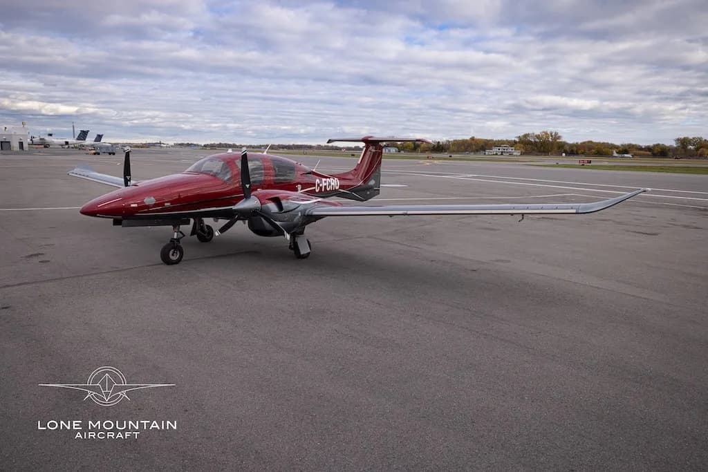 A red and grey Diamond DA62 aircraft with registration C-FCRQ parked on an airfield, viewed from the front.