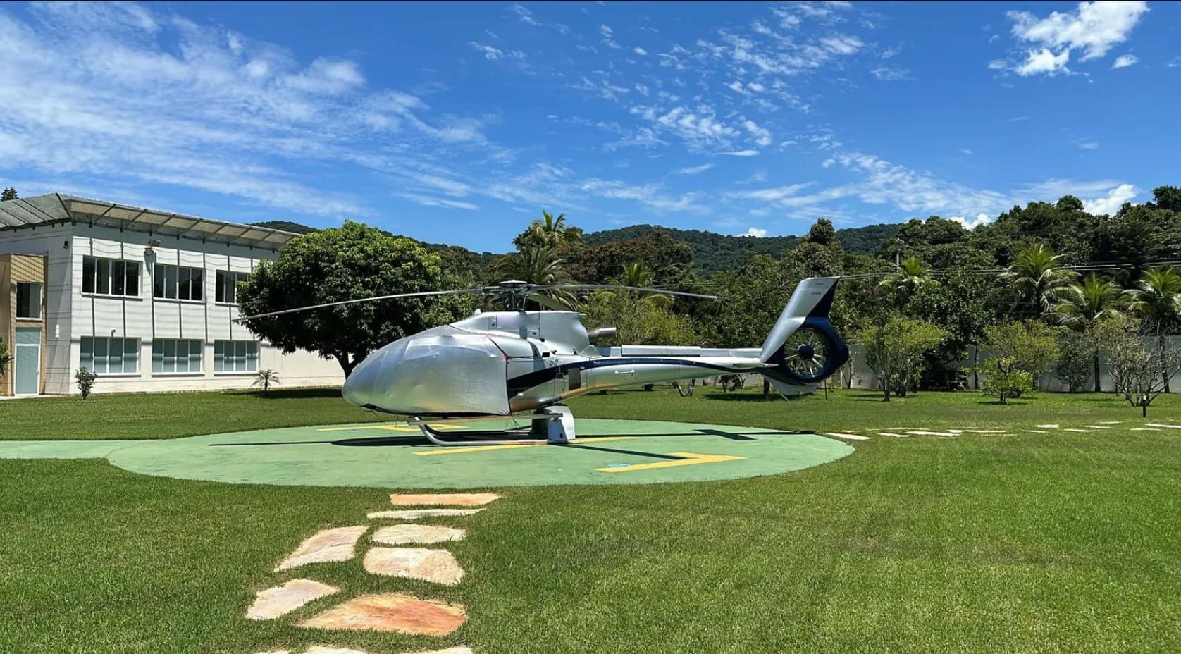 A silver Eurocopter EC130 B4 helicopter parked on a helipad.