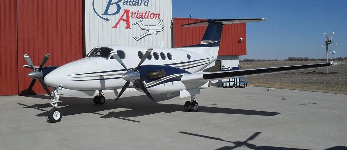 A King Air aircraft is parked in front of a hangar with the company logo.