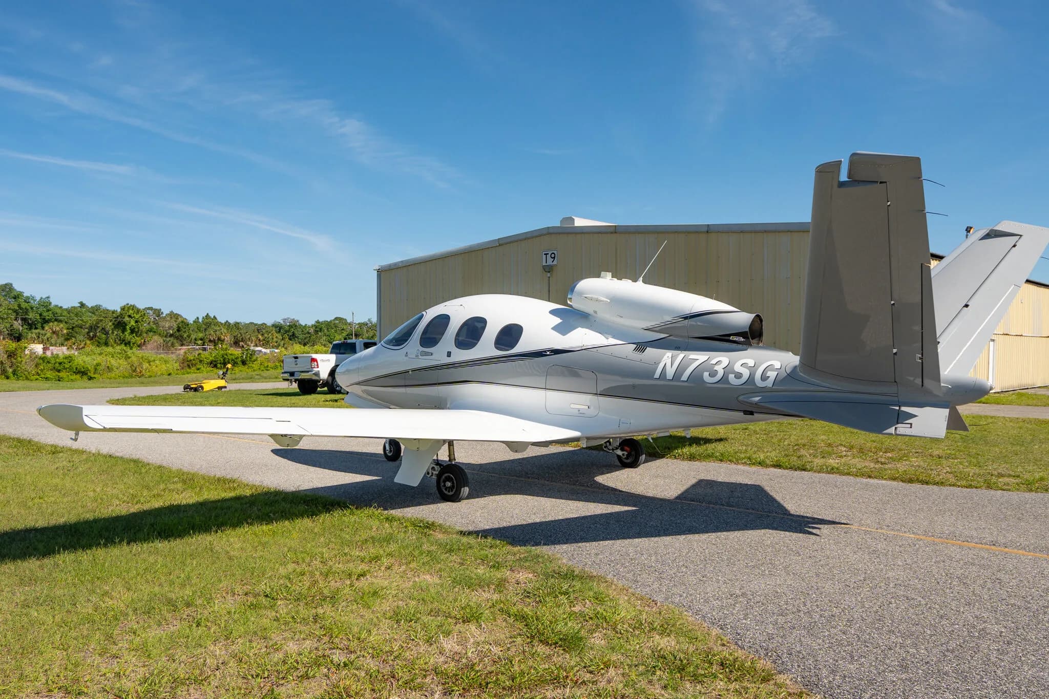 Side view of a white and grey Cirrus Vision Jet N73SG parked on an airfield.
