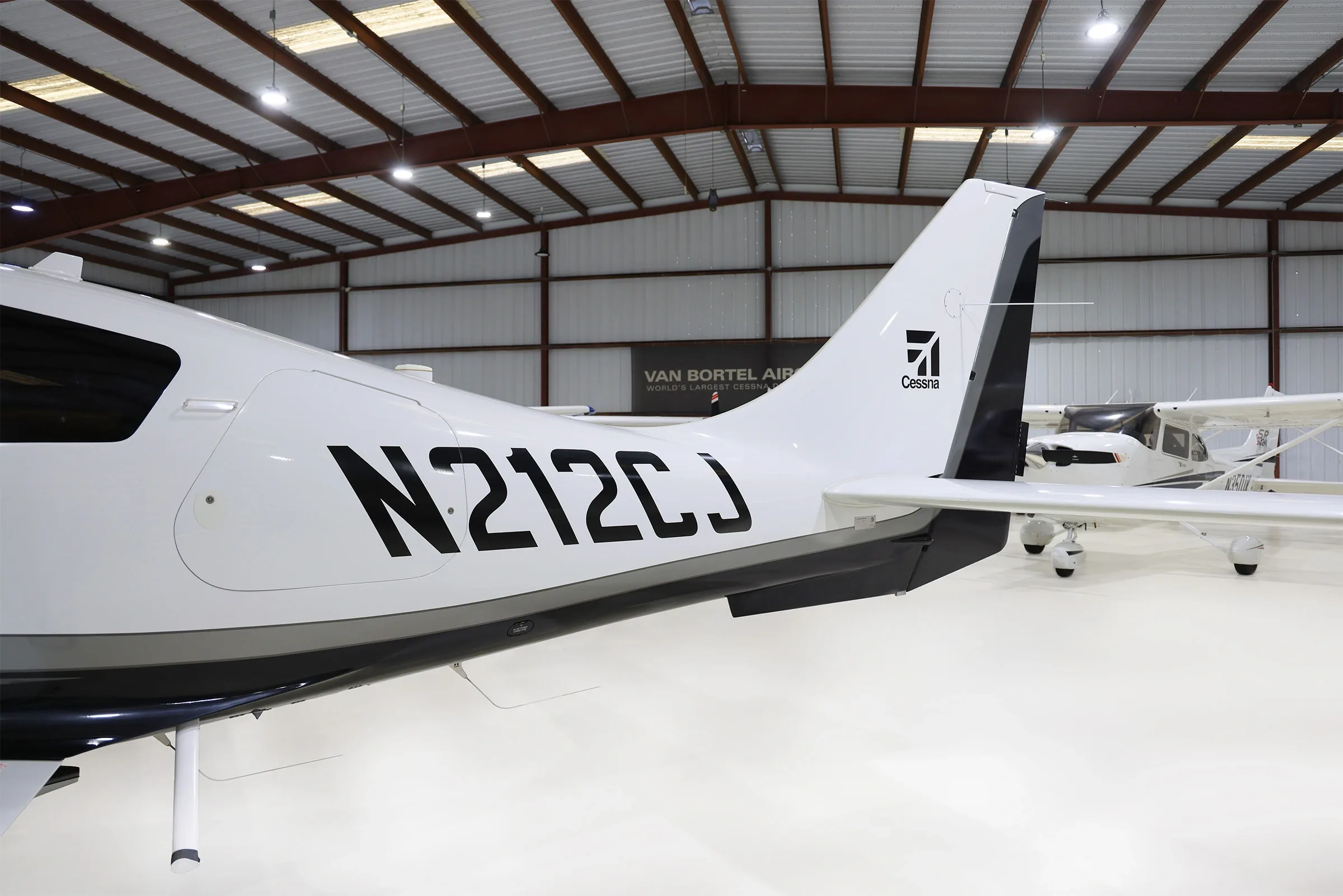 A close-up view of the tail section of a white and black Cessna TTx aircraft (N212CJ) in a hangar.