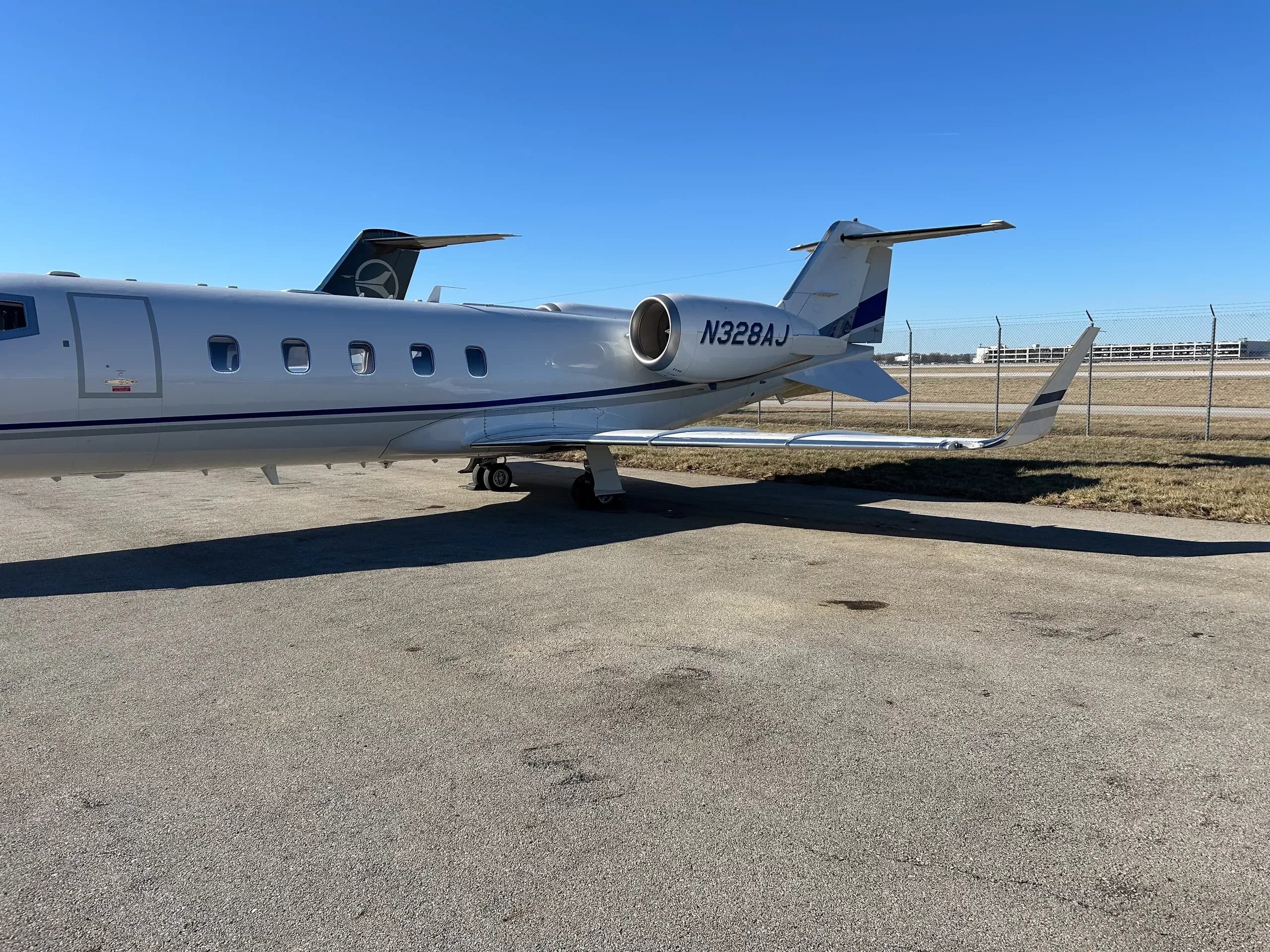 A side view of the white Learjet N328AJ with blue stripes parked on an airport tarmac.