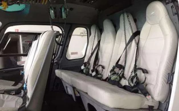 The interior of the helicopter features white leather seats and black seatbelts.