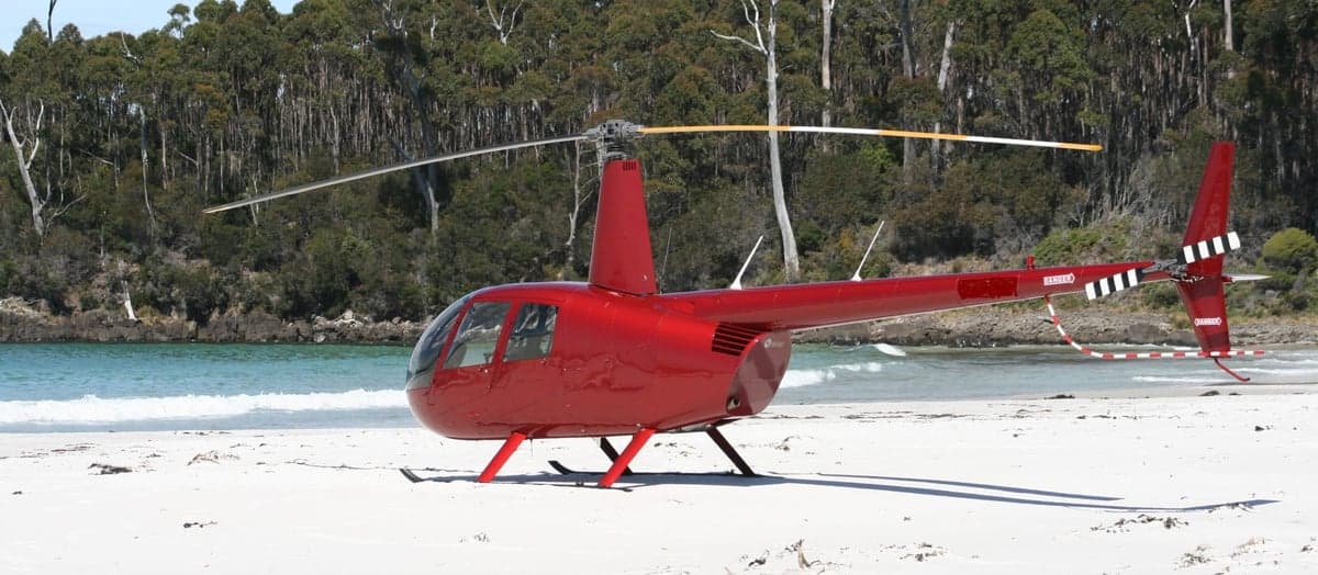 A red Robinson helicopter parked on a sandy beach.