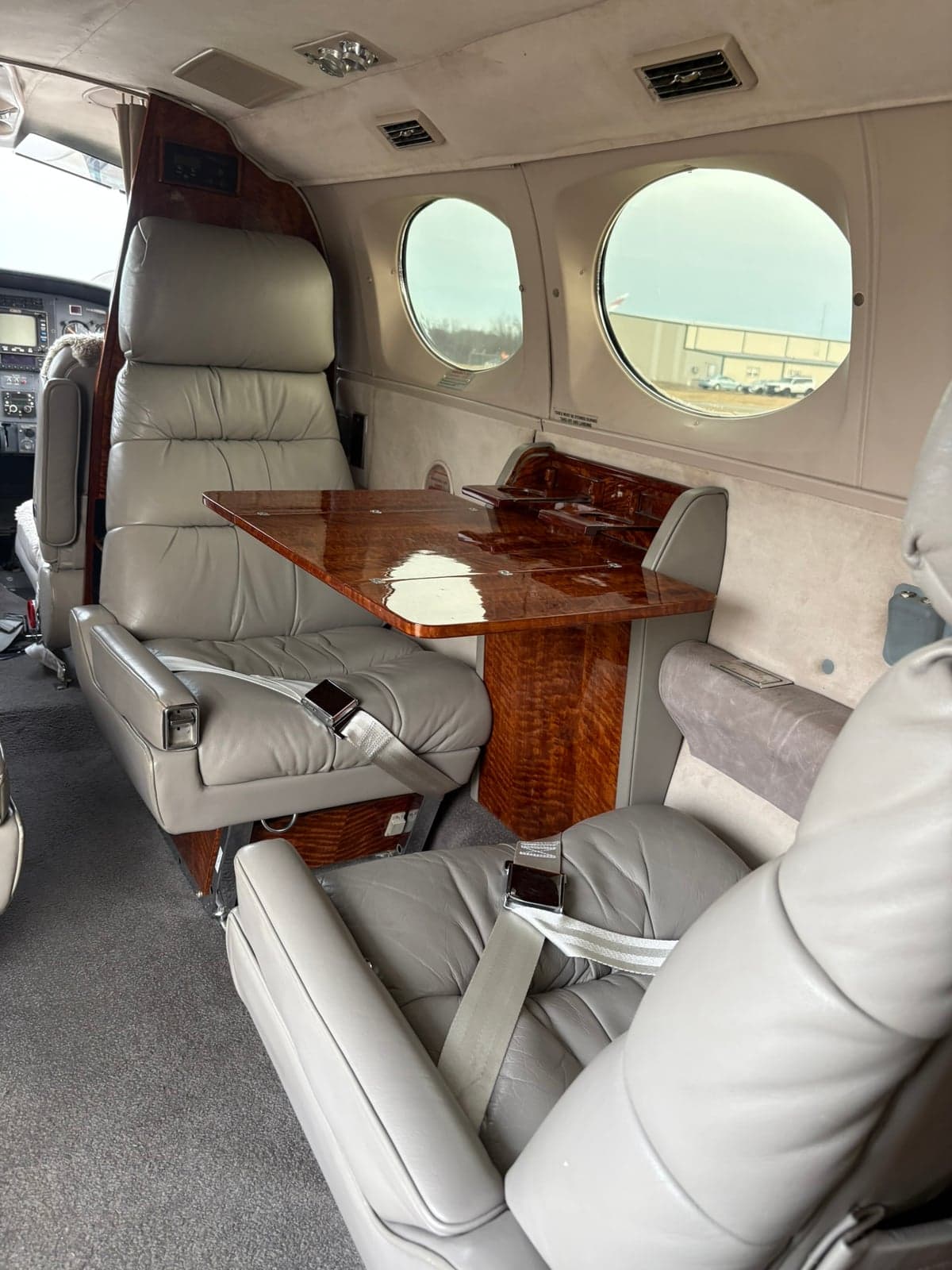Aircraft cabin interior with grey leather seats and a polished wooden fold-out table.