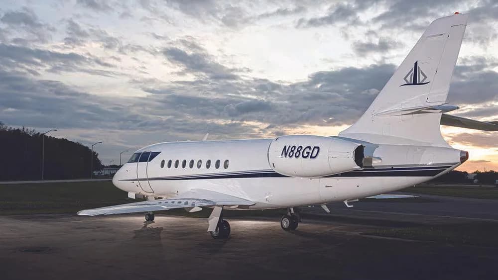 A rear-quarter view of the white business jet N88GD with a dark blue stripe, parked on an tarmac at sunset.