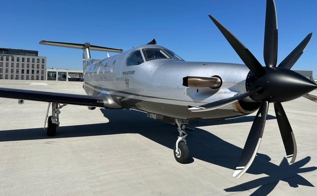 Pilatus PC-12 aircraft D-FCYW on the tarmac with a silver and black paint scheme.