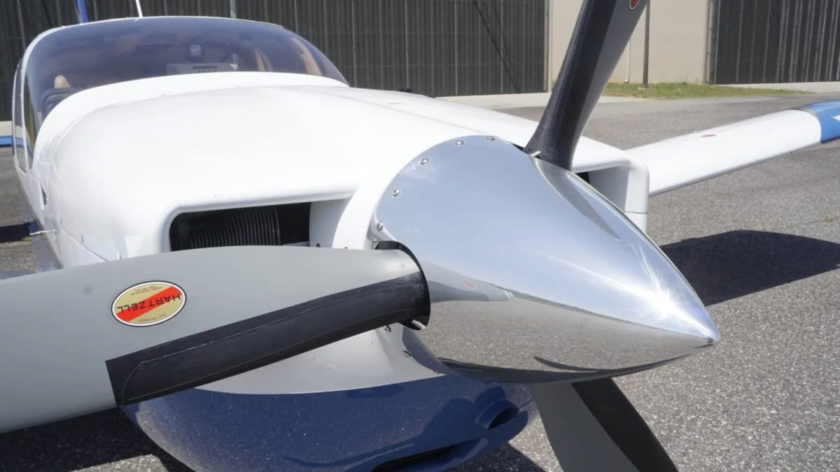 A close-up view of the propeller and nose of a white and blue aircraft, showing the Hartzell propeller.