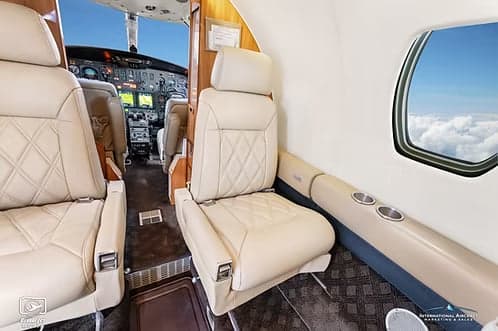 A view from the business jet cabin shows light-colored leather seats and a glimpse of the cockpit.