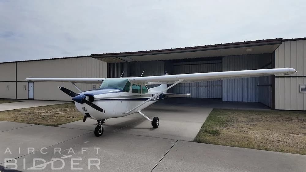 A white and blue Cessna 172 Skyhawk aircraft (N13236) parked on an apron in front of a hangar.