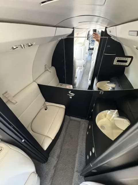The interior of a business jet, showing a private area with a mirror and light-colored seating.