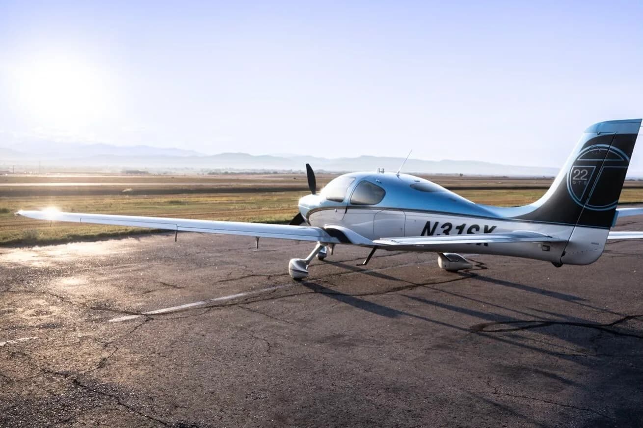 A Cirrus SR22T aircraft, N31SX, in blue and silver paint, parked on an airfield with a bright sun flare.