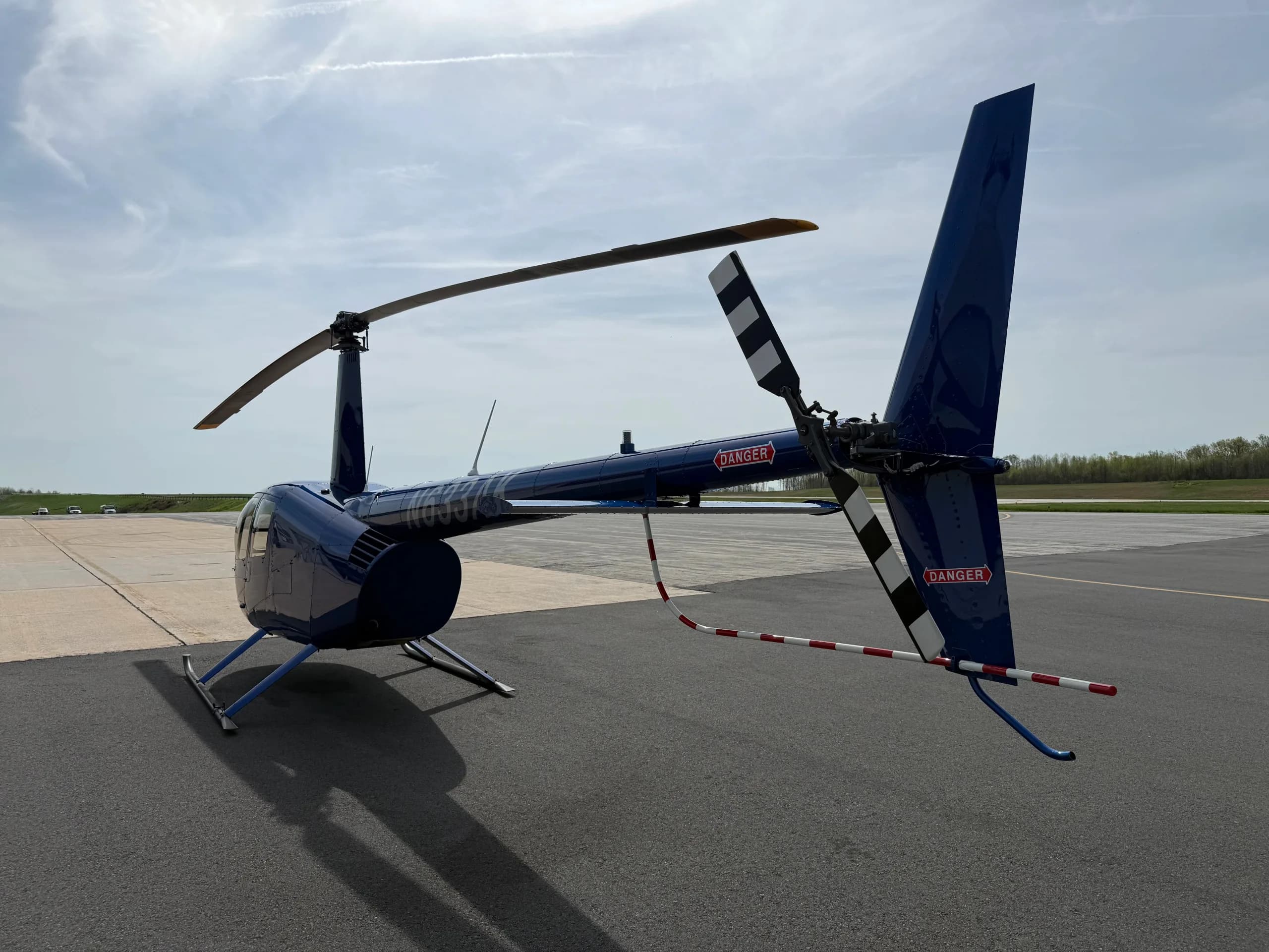 A rear three-quarter view of a blue Robinson R44 helicopter, N633AK, showing the tail rotor and skid landing gear.