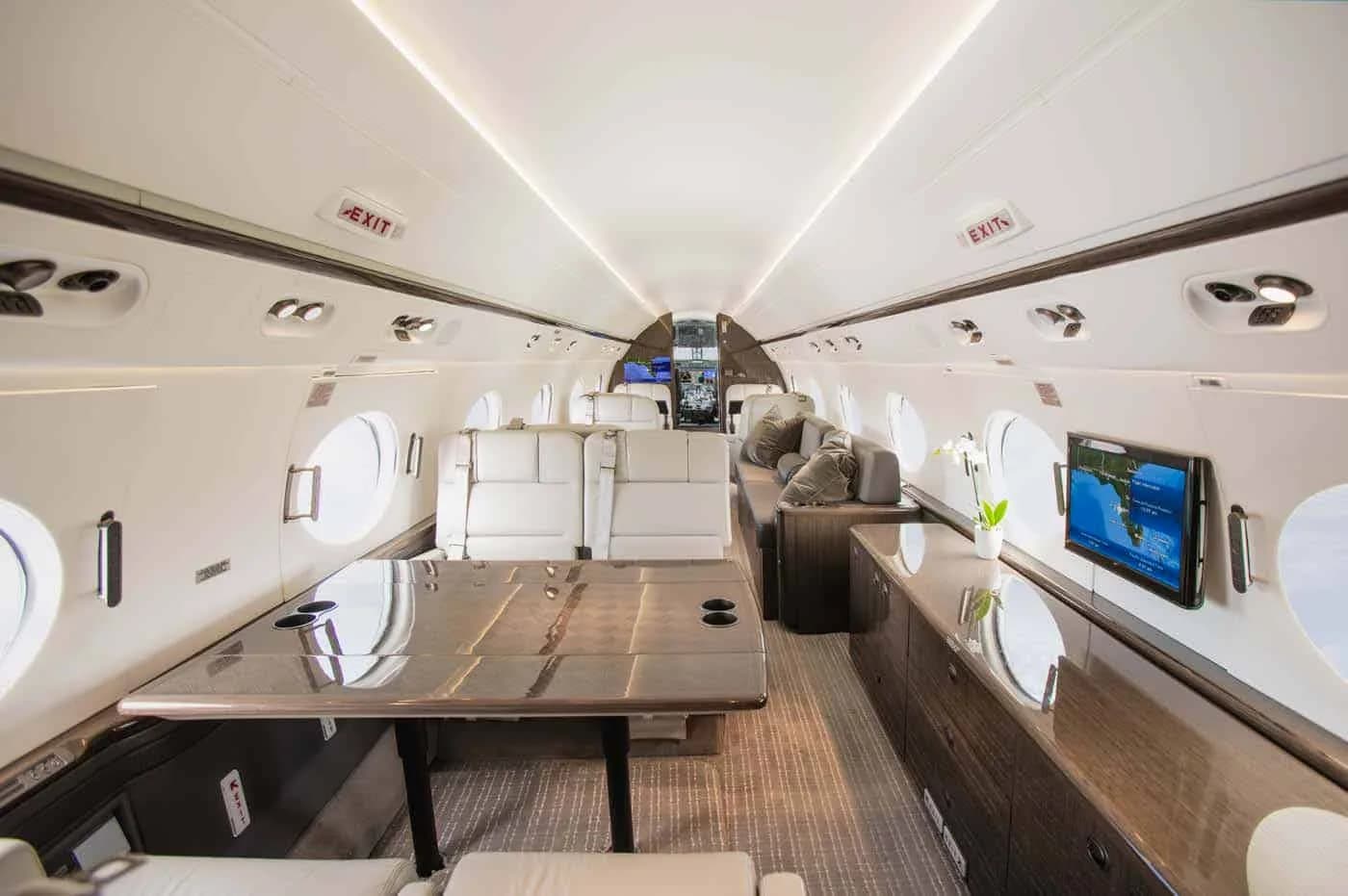 A wide view of a luxurious aircraft cabin with a large table, light-colored seating, and dark wood accents.