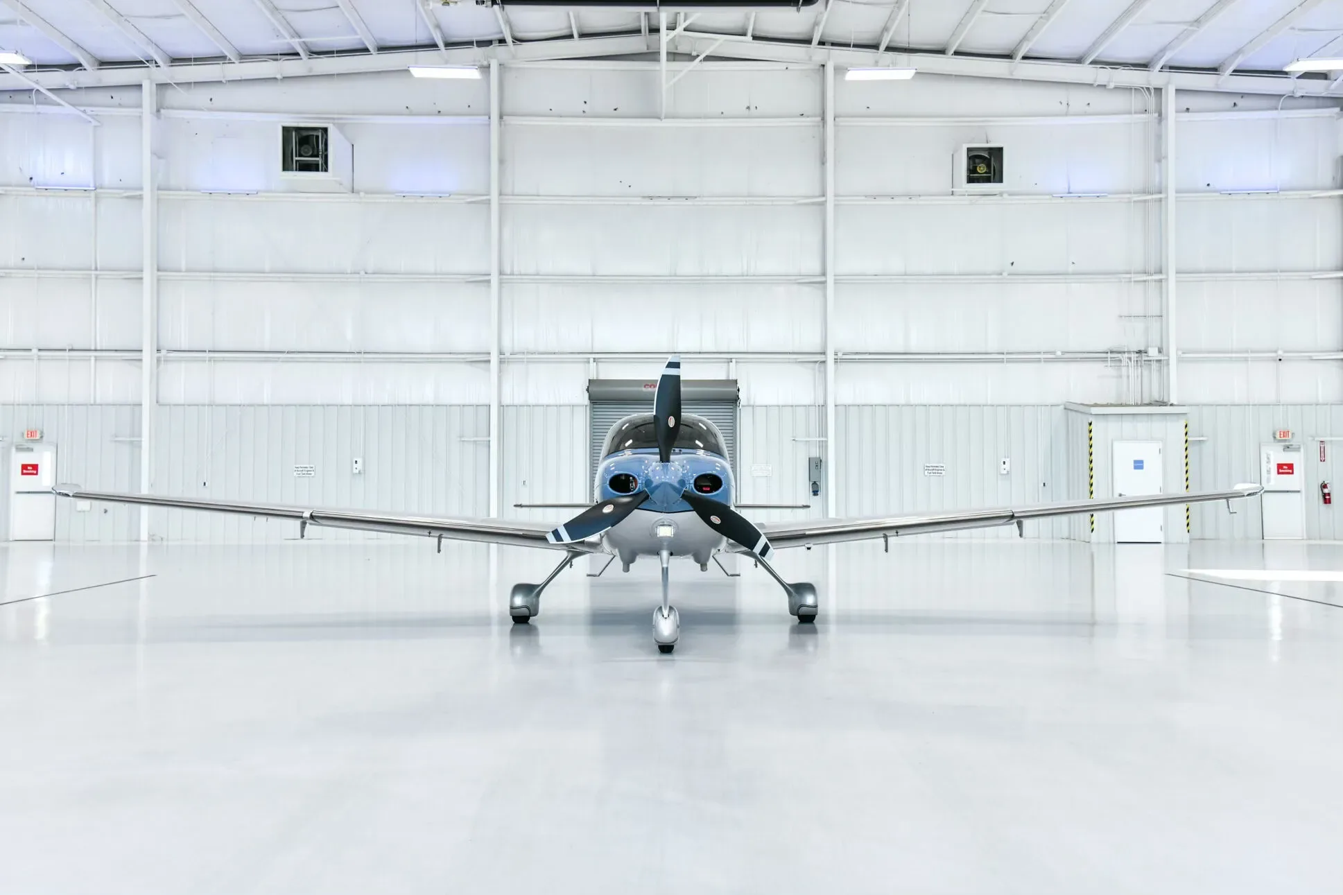 A blue and white Cirrus SR22 aircraft with registration N322LT viewed head-on in a brightly lit hangar.