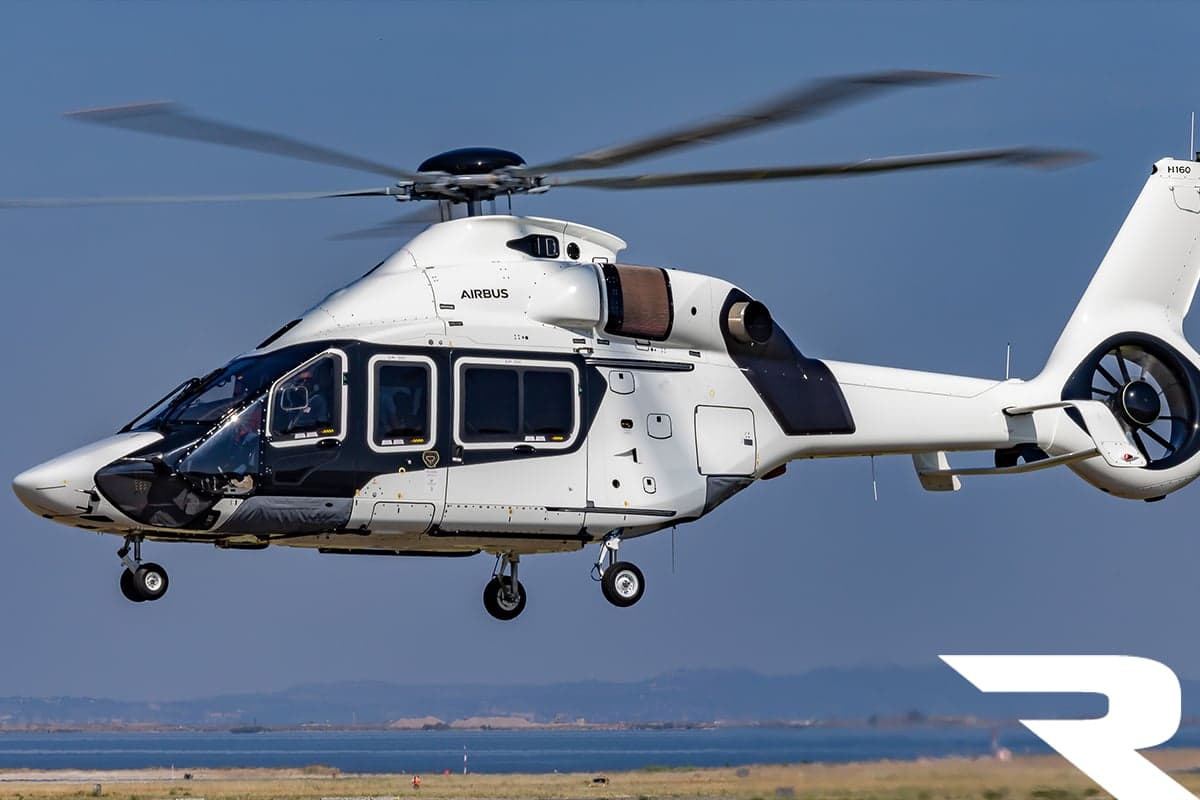 A white and black Airbus H160 helicopter hovers over a coastal landscape.