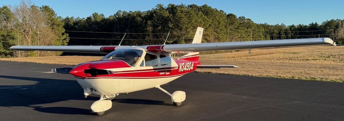 A Cessna Cardinal aircraft with red and white paint scheme is parked on the tarmac.