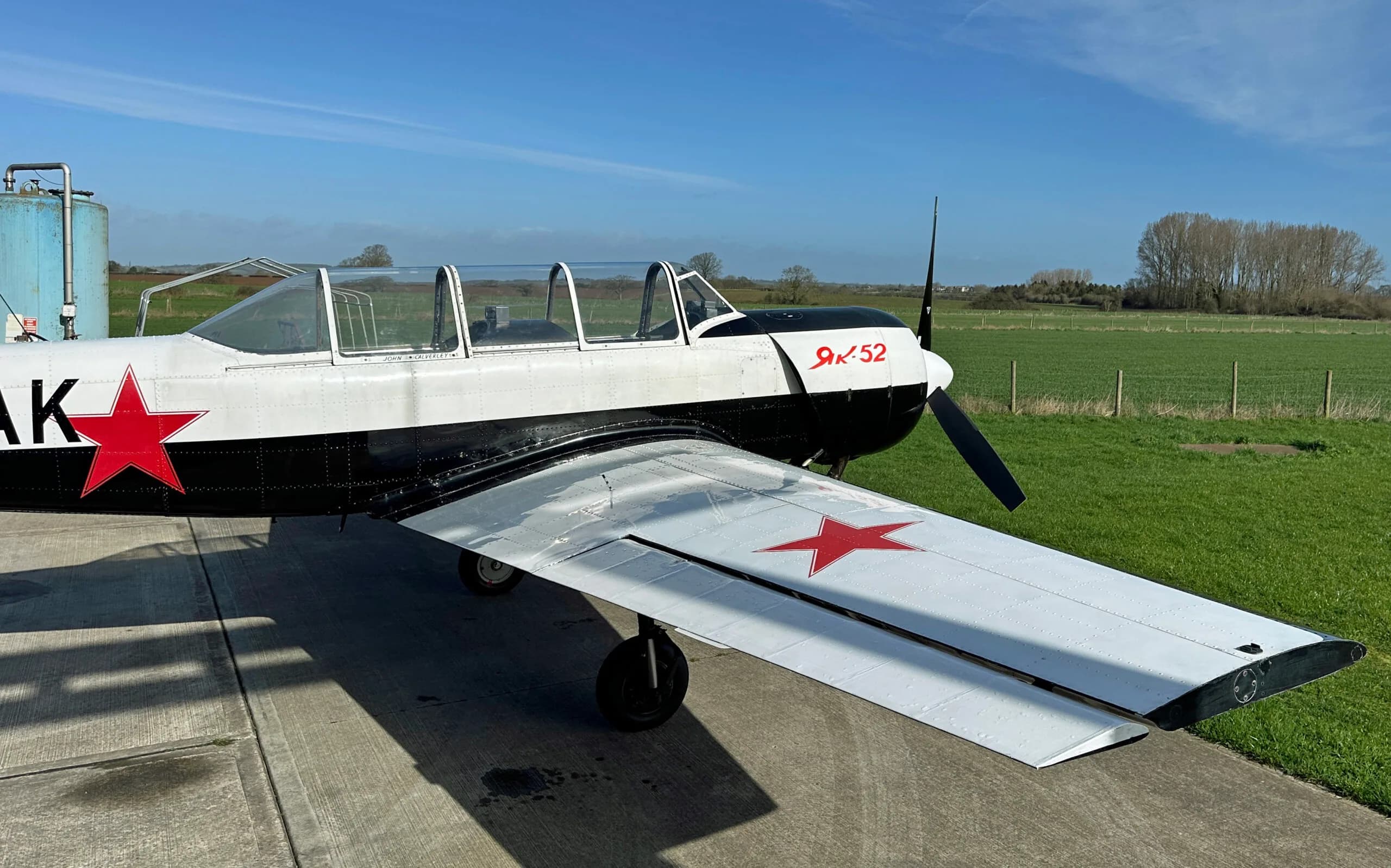 A side view of a white and black Yak-52 aircraft, highlighting the wing with a red star and the propeller.