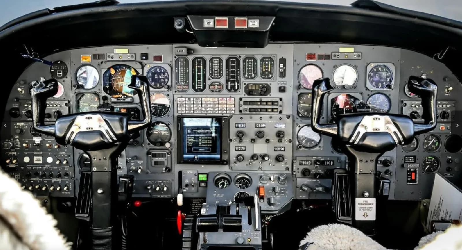 The cockpit of a business jet with a complex instrument panel, multiple gauges, and two control yokes.