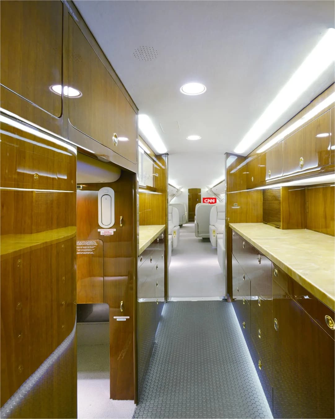 A long view of a private jet's galley area with extensive wooden cabinetry and light-colored countertops.