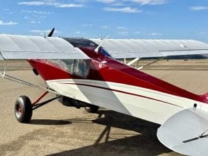 Side view of a red and white Carbon Cub aircraft on the ground.