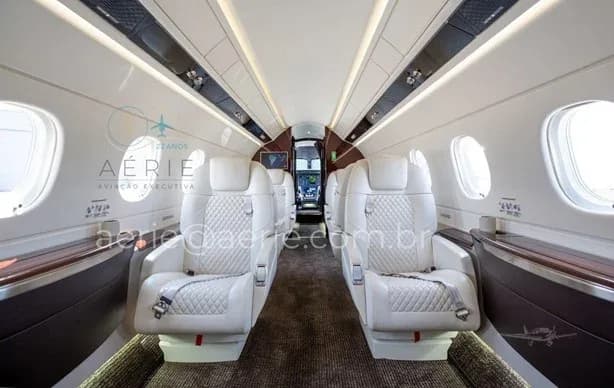 The aircraft's elegant cabin interior with rows of white quilted seats and overhead lighting.
