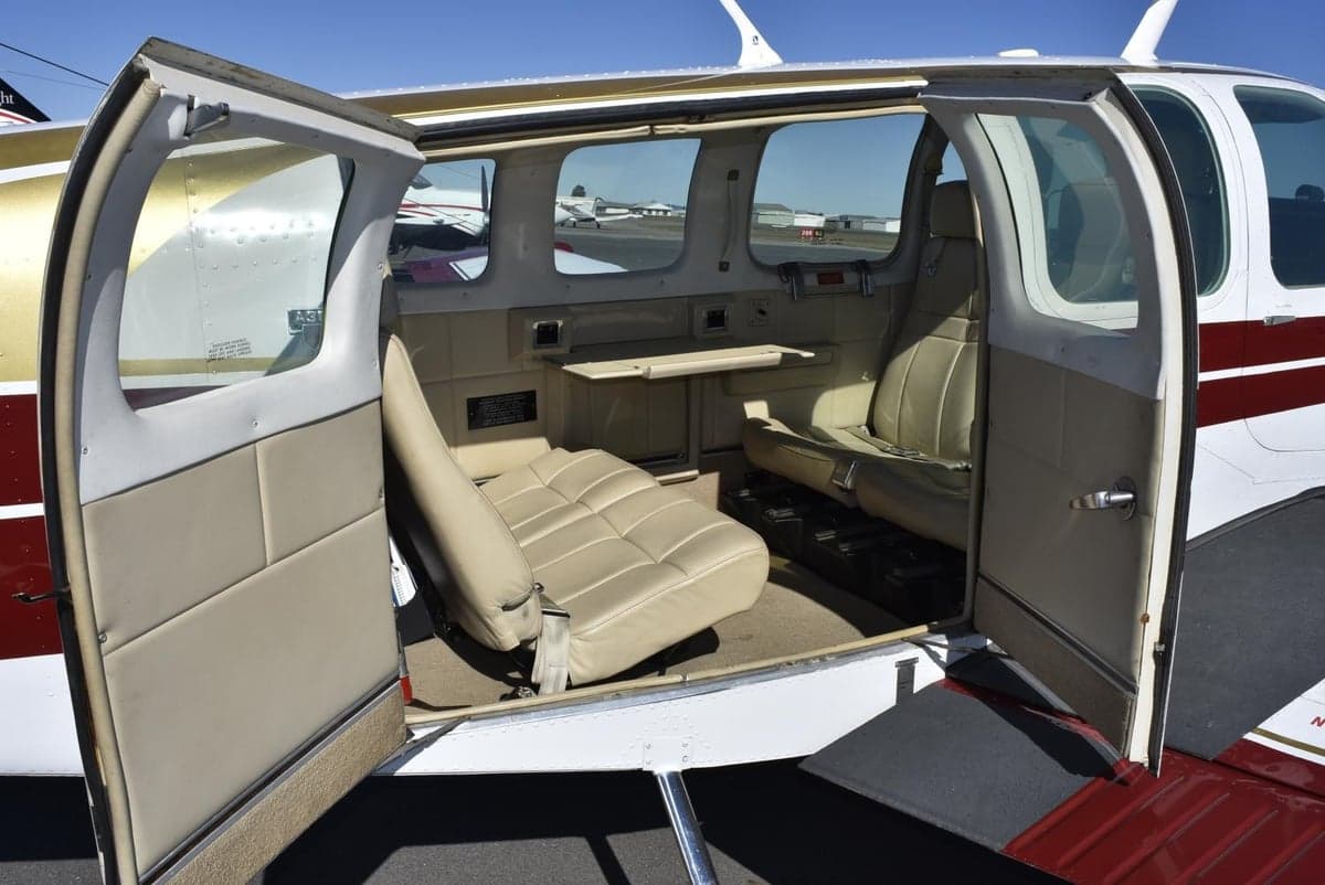 The open cabin door of a small aircraft revealing beige interior seats and other aircraft outside.