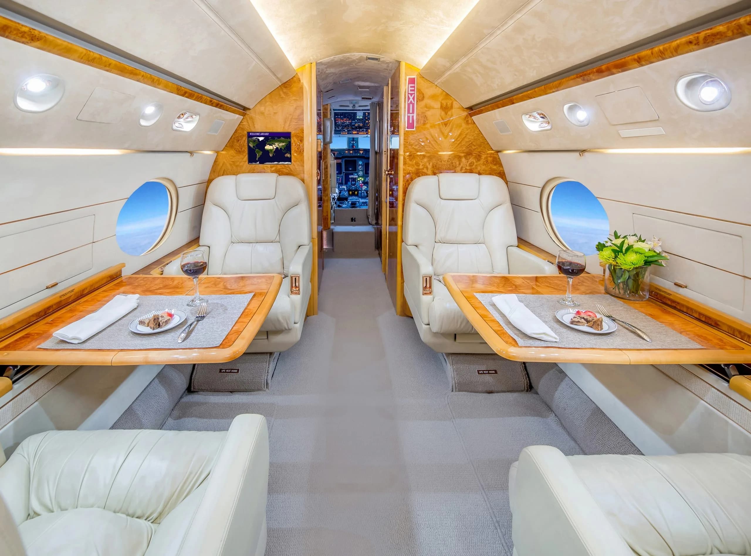 Aircraft interior with cream-colored leather seats and wood tables set for dining.