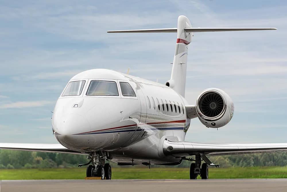 A three-quarter front view of a white business jet with red and blue stripes, parked on an airfield.