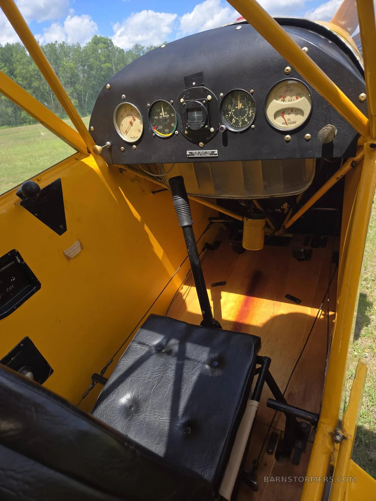 A close-up view of the simple instrument panel and wooden floor of a yellow aircraft's cockpit.