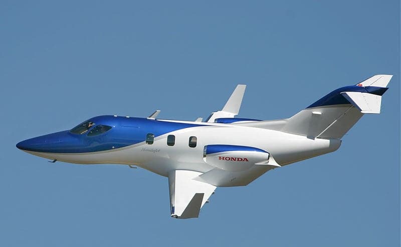 A blue and white HondaJet aircraft is in flight against a clear blue sky.