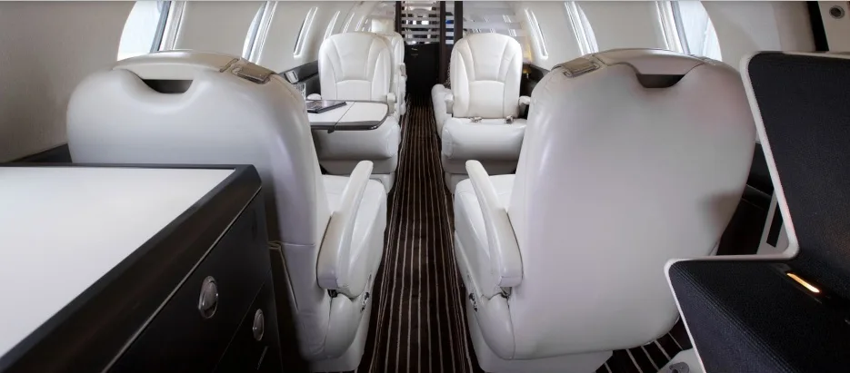 A perspective view down the aisle of a private jet cabin shows rows of white leather seats.