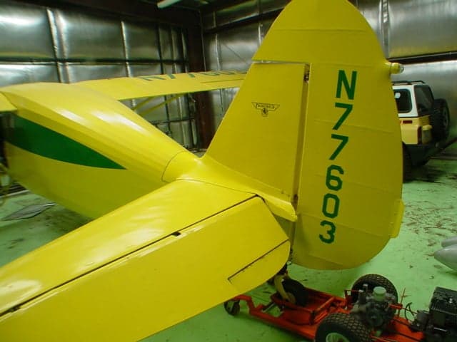 Close-up of the yellow tail of a Fairchild 24 aircraft with green registration N77603 inside a hangar.