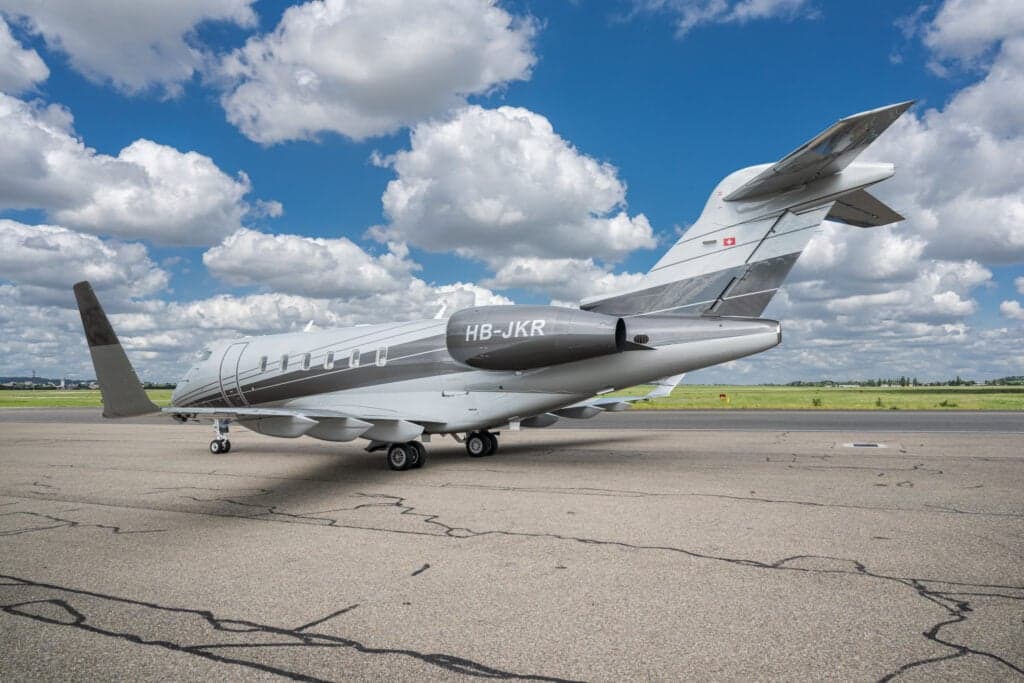 A Challenger aircraft with registration HB-JKR is parked on the tarmac, showing the tail and rear of the fuselage.