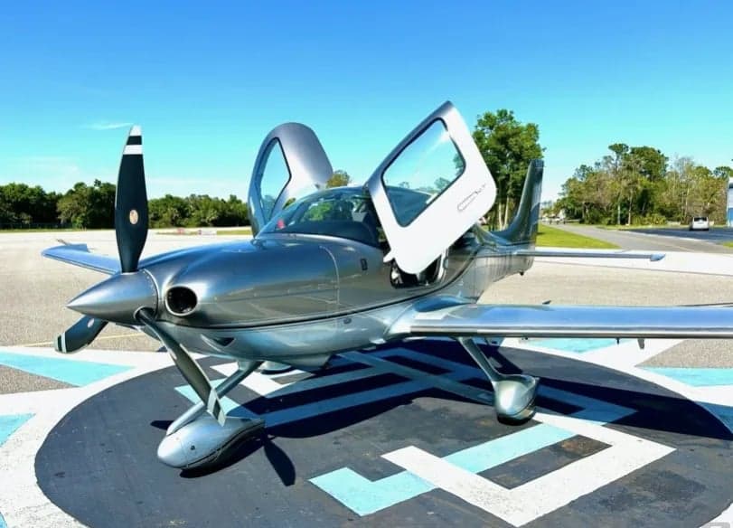 Front view of the silver Cirrus aircraft with its doors open.