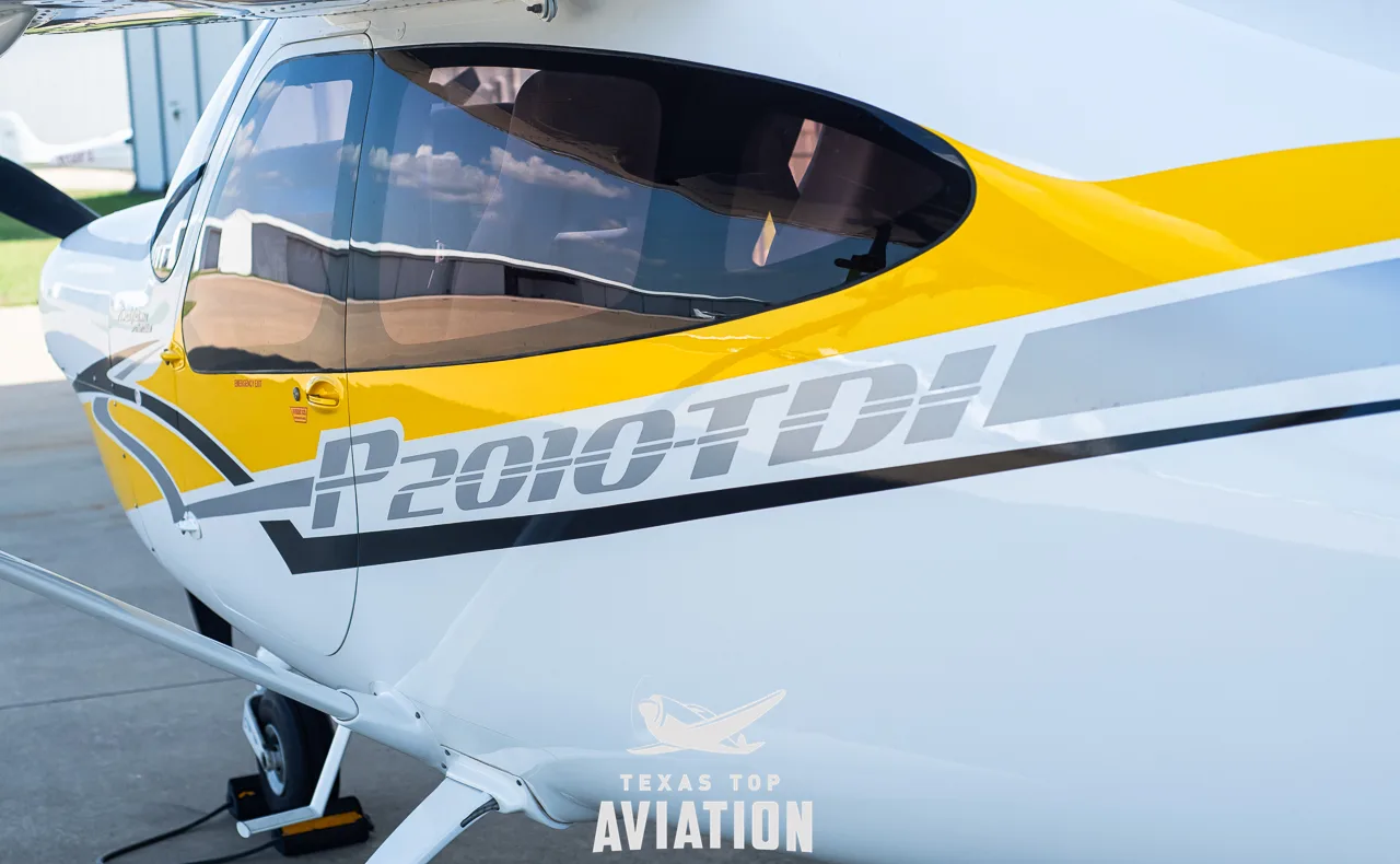 A close-up of the fuselage of a white and yellow Tecnam P2010 TDI aircraft, highlighting the model name.
