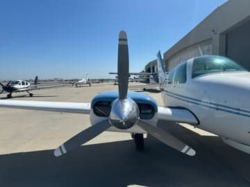 A Beechcraft Bonanza with blue and white paint scheme is parked outside a hangar.